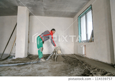 A builder in work clothes is doing his job, leveling the floor, pouring mortar A builder in work clothes is doing his job, leveling the floor, pouring mortar 114339757