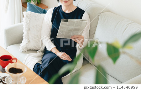 A woman reading an English newspaper in the living room A woman reading an English newspaper in the living room 114340959