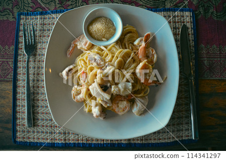Overhead view of a plate of creamy shrimp pasta topped with parmesan cheese on a patterned tablecloth Overhead view of a plate of creamy shrimp pasta topped with parmesan cheese on a patterned tablecloth 114341297