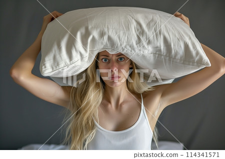 Young woman covering ears with pillow because of noise. 114341571