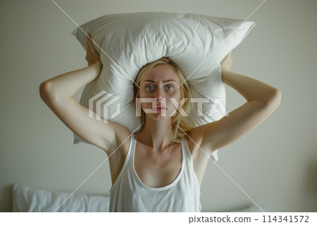 Young woman covering ears with pillow because of noise. Young woman covering ears with pillow because of noise. 114341572