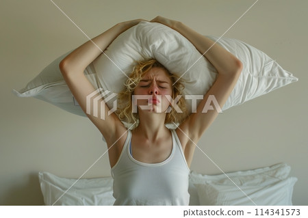 Young woman covering ears with pillow because of noise. 114341573