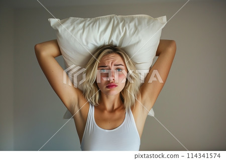 Young woman covering ears with pillow because of noise. Young woman covering ears with pillow because of noise. 114341574