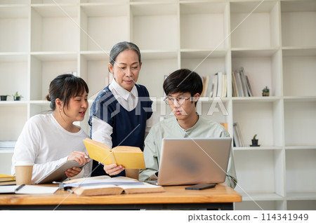 A mature Asian female professor helping her students in the classroom, explaining some hard topics. A mature Asian female professor helping her students in the classroom, explaining some hard topics. 114341949