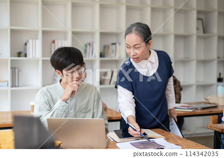 A mature Asian female teacher helping and explaining difficult math problems to her student. 114342035