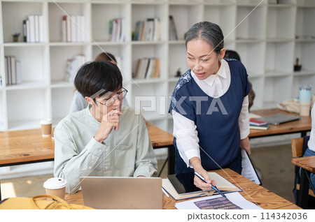 A mature Asian female teacher helping and explaining difficult math problems to her student. A mature Asian female teacher helping and explaining difficult math problems to her student. 114342036