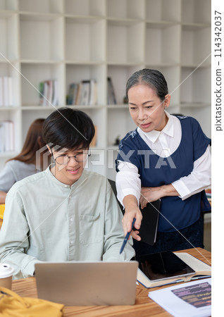 A mature Asian female teacher helping and explaining difficult math problems to her student. A mature Asian female teacher helping and explaining difficult math problems to her student. 114342037