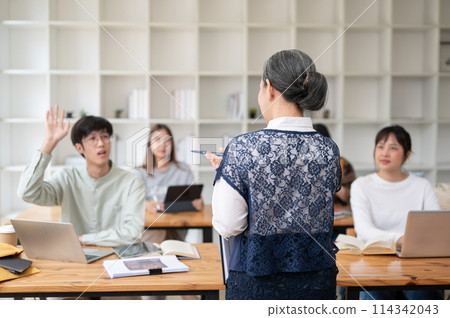 A back view image of a teacher professor giving a lecture to her students in the classroom. A back view image of a teacher professor giving a lecture to her students in the classroom. 114342043