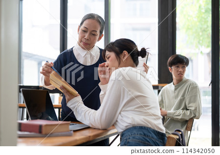 Senior Asian female teacher helping and explaining difficult math problems to her student. Senior Asian female teacher helping and explaining difficult math problems to her student. 114342050