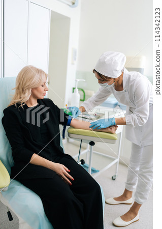 Vertical shot of nurse in medical gloves wiping with cotton wool vein, wipes place where will take blood for analysis. Doctor prepares patient hand to draw blood from vein. Preparation for blood test 114342123