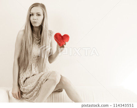 Sad woman holding red pillow in heart shape 114343551