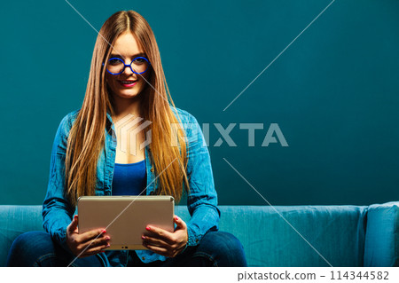 woman with tablet sitting on couch blue color woman with tablet sitting on couch blue color 114344582