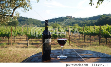 Scenic vineyard view with a red wine bottle and glass on table in Tuscany, Italy 114344702