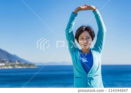 Senior woman stretching with the sea in the background 114344847