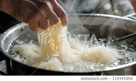 Close-up of man's hand cooking shirataki noodle in pan. 114345800