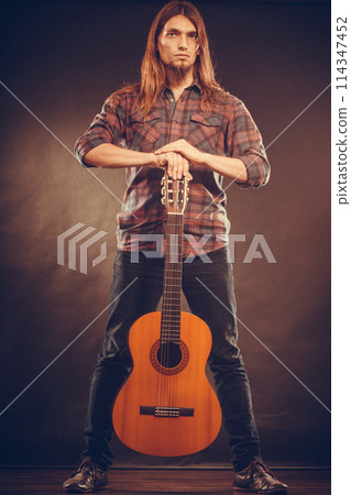 Young man is standing and holding his guitar. 114347452