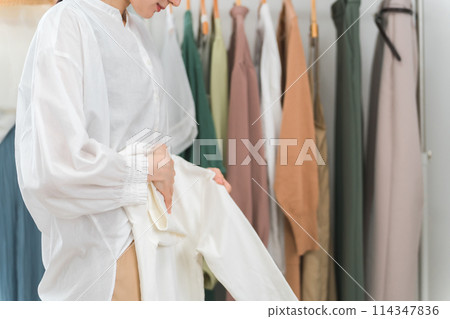 Hands of an Asian woman in a shop folding clothes, a salesperson working in a clothing store, an employee, a shop assistant Hands of an Asian woman in a shop folding clothes, a salesperson working in a clothing store, an employee, a shop assistant 114347836