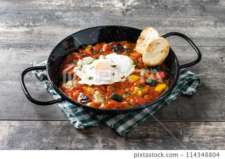 Eggplant and egg, onions, peppers, served in frying pan on wooden table, Vegetable pisto manchego with tomatoes, zucchini 114348804