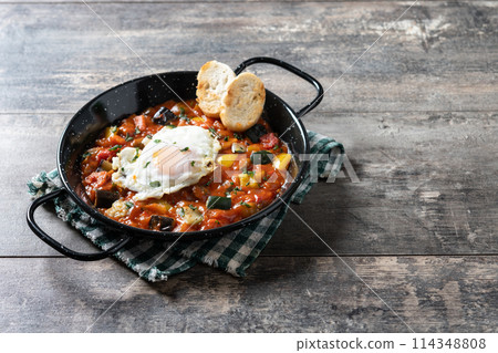 Eggplant and egg, onions, peppers, served in frying pan on wooden table, Vegetable pisto manchego with tomatoes, zucchini 114348808