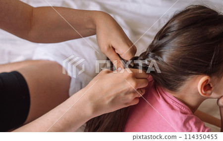 Mom braids her daughter's hair while sitting in bed 114350455