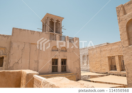 House in traditional Arabic architecture with wind tower. Traditional Arabic style building with windcatcher tower and palm leaves thatched roof. Old Dubai, UAE. View of rooftops of old Arab city 114350568