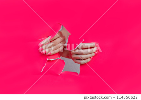 female hands with beautiful nails with pink manicure in pink paper hole 114350622