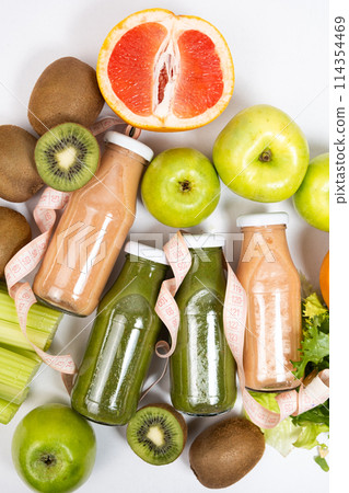 Healthy bottled smoothies among vegetables and fruits and measuring tape. 114354469
