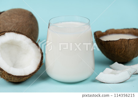 Healthy vegan coconut milk in a glass and coconut shell on a blue background. Healthy vegan coconut milk in a glass and coconut shell on a blue background. 114356215