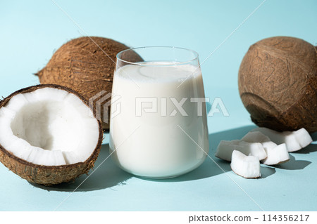 Coconut milk in a glass among coconuts on a blue background Coconut milk in a glass among coconuts on a blue background 114356217