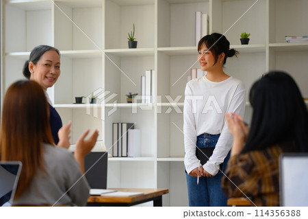 Smiling Asian student woman having presentation while her classmates giving applause Smiling Asian student woman having presentation while her classmates giving applause 114356388