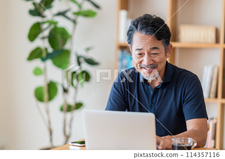 A senior man invests in stocks in his living room. 114357116