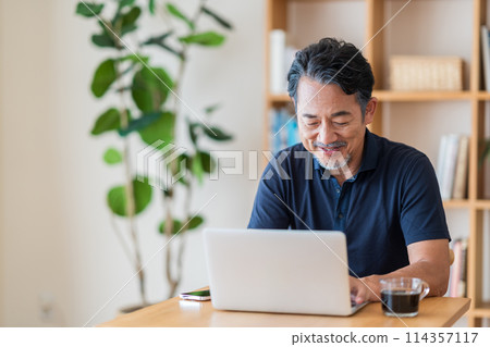 A senior man invests in stocks in his living room. 114357117