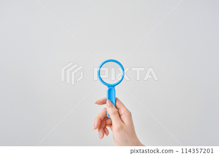 Woman's hand holding a magnifying glass and a white background 114357201