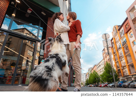 Young couple, man and woman flirting at the street. Family walking together in city with Aussie dog. Bottom view Young couple, man and woman flirting at the street. Family walking together in city with Aussie dog. Bottom view 114357644