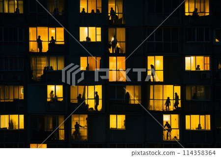 Silhouetted Figures in Lit Windows of Urban Apartment Building at Dusk 114358364