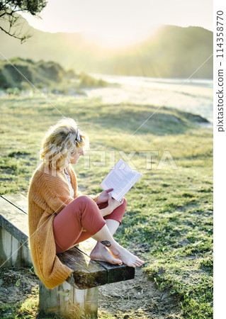 Young mature blonde woman reading outdoor. 114358770