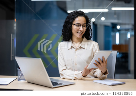 Young successful businesswoman at workplace is satisfied with results of achievement at work smiling and using tablet computer, programmer is testing new software in application Young successful businesswoman at workplace is satisfied with results of achievement at work smiling and using tablet computer, programmer is testing new software in application 114358895