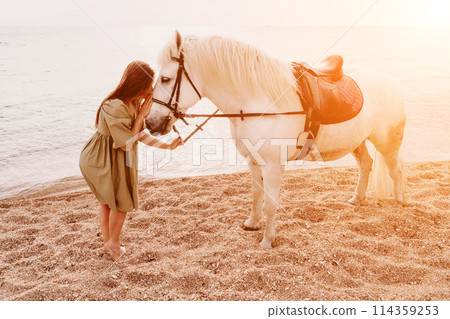 A woman in a dress stands next to a white horse on a beach, with the blue sky and sea in the background. A woman in a dress stands next to a white horse on a beach, with the blue sky and sea in the background. 114359253