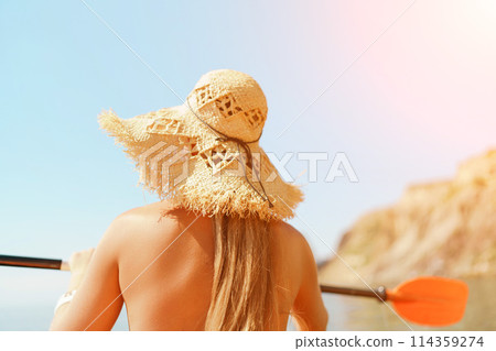 A woman wearing a straw hat is paddling a canoe on a sunny day. Scene is relaxed and carefree, as the woman enjoys her time on the water. 114359274