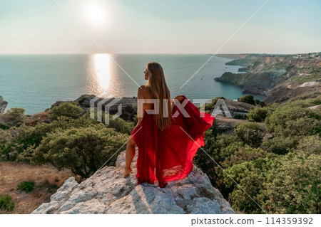 Woman sunset sea red dress, back view a happy beautiful sensual woman in a red long dress posing on a rock high above the sea on sunset. Woman sunset sea red dress, back view a happy beautiful sensual woman in a red long dress posing on a rock high above the sea on sunset. 114359392