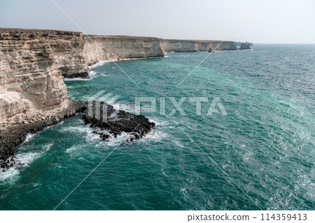 The ocean is calm and the shoreline is rocky. The water is a deep blue color. The rocks are jagged and the waves are small. The scene is peaceful and serene. The ocean is calm and the shoreline is rocky. The water is a deep blue color. The rocks are jagged and the waves are small. The scene is peaceful and serene. 114359413
