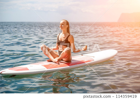 Woman sup sea. Sports girl on a surfboard in the sea on a sunny summer day. In a black bathing suit, he sits on a sapa in the sea. Rest on the sea. 114359419