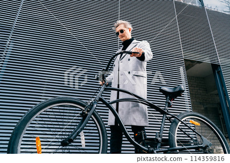 Stylish male in checked coat and sunglasses walking with retro bicycle near gray urban wall in sunny day. Neutral carbon footprint transportation. Green eco friendly mobility sustainable transport Stylish male in checked coat and sunglasses walking with retro bicycle near gray urban wall in sunny day. Neutral carbon footprint transportation. Green eco friendly mobility sustainable transport 114359816