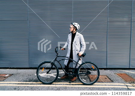 Stylish male in coat, sunglasses and protective helmet standing with retro bicycle near gray urban wall. Neutral carbon footprint transportation. Green eco friendly mobility sustainable transport Stylish male in coat, sunglasses and protective helmet standing with retro bicycle near gray urban wall. Neutral carbon footprint transportation. Green eco friendly mobility sustainable transport 114359817