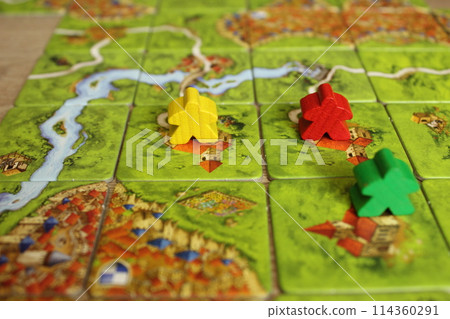 Mozyr, Belarus, April 03 2024: board family game carcassonne green yellow red meeple on the map tiles of the playing field. Rules for placing monasteries on carriages 114360291