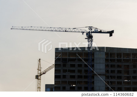Construction cranes on top of a building under construction. The cranes are engaged in the construction work of the building. 114360682