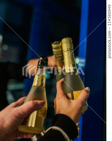 Close up of two hands holding bottles of champagne in the night club 114360949