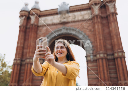 Young female tourist visiting Barcelona triumphal arch. Traveling woman taking selfie outdoors. Banner of travel, tourism and vacation in city. Use technology concept, Traveling Europe 114361556