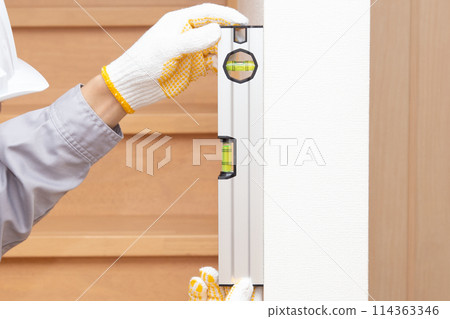 A worker uses a level to check the verticality of a wall A worker uses a level to check the verticality of a wall 114363346