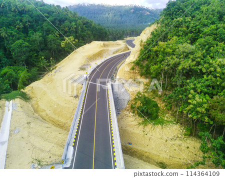 a curved road snaking through a dense green forest. 114364109